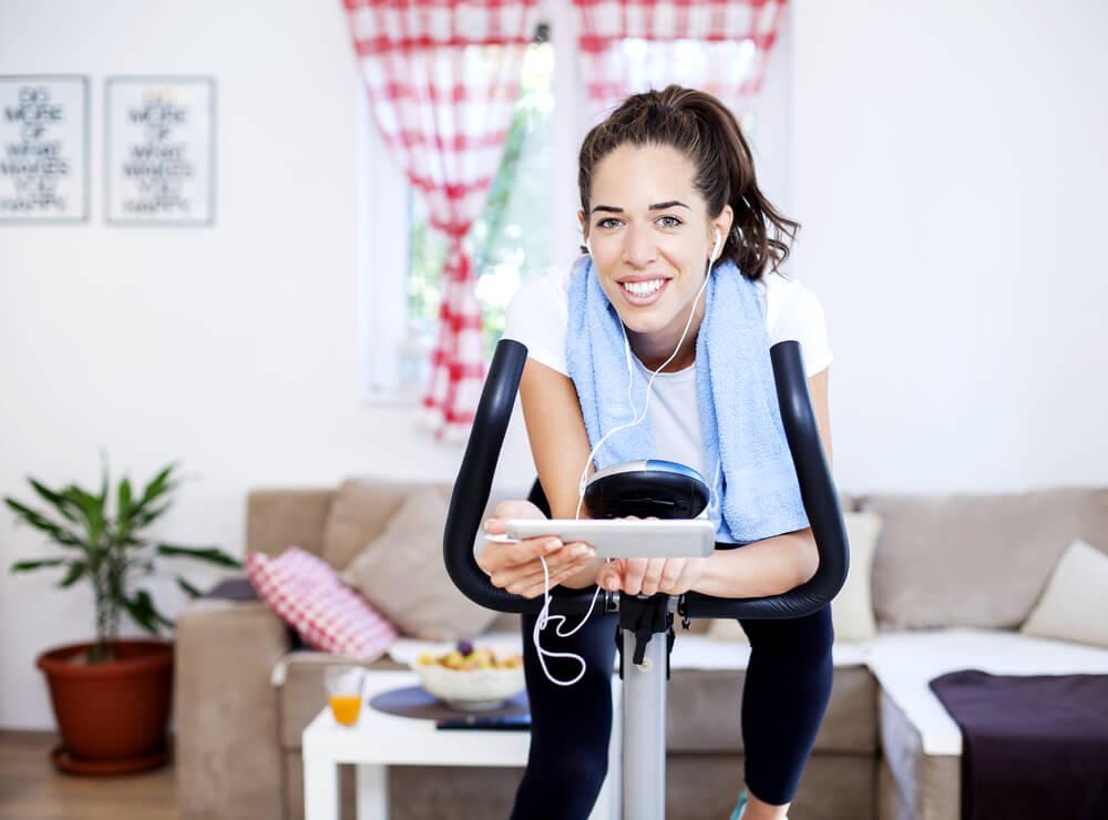 Woman on exercise bike with tablet and earphones