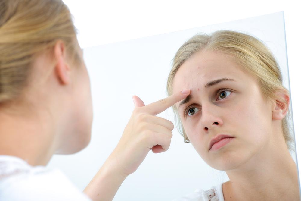 Woman examining her pimple in the mirror.