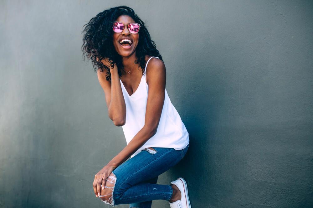 Laughing woman with pink sunglasses leaning against wall