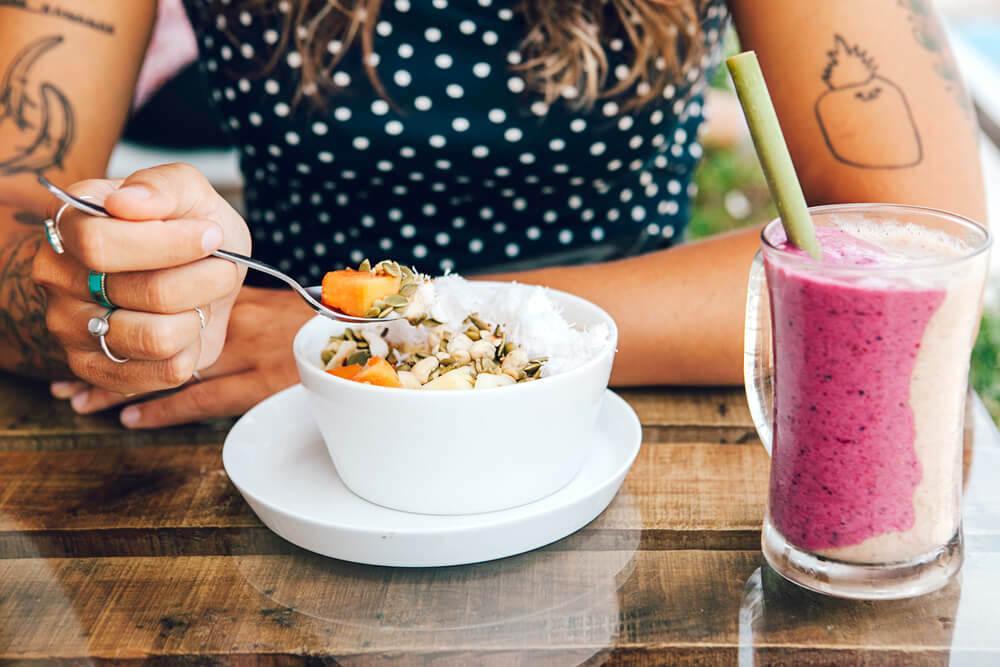 Unknown woman eating granola in a bowl, with a pink smoothie