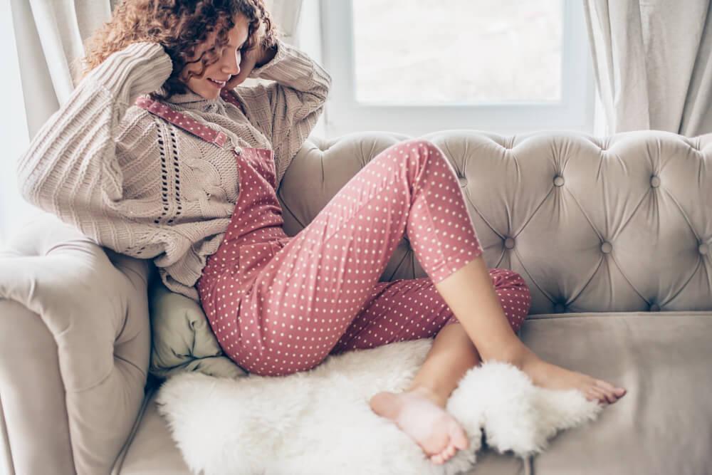 Woman wearing overalls over a jumper sitting on sofa